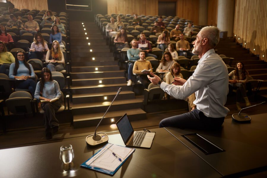 Senior professor talking in front of large group of his students during a lecture in amphitheater.